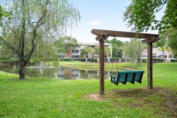 A wooden swing set sits in a grassy area next to a pond.